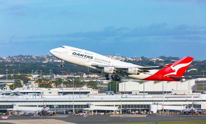 a Qantas 747 taking off from Sydney airport with the terminal building in the background.